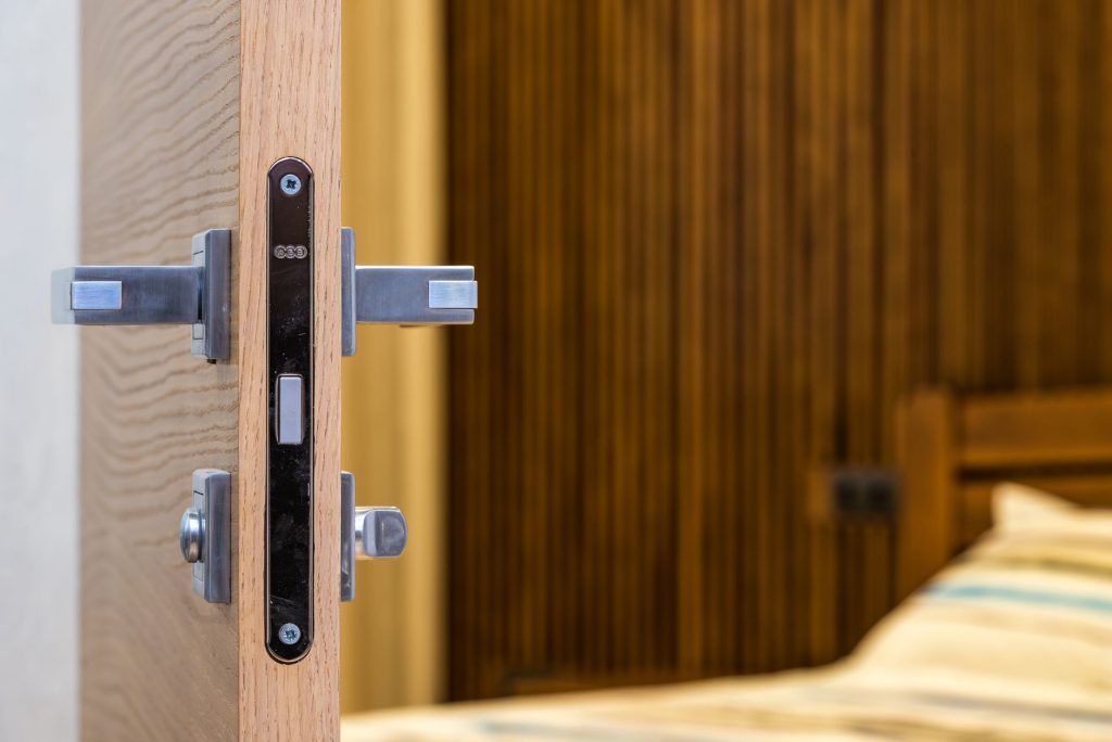 Opened doorway with lock and simple metal handle in light room with wooden bed