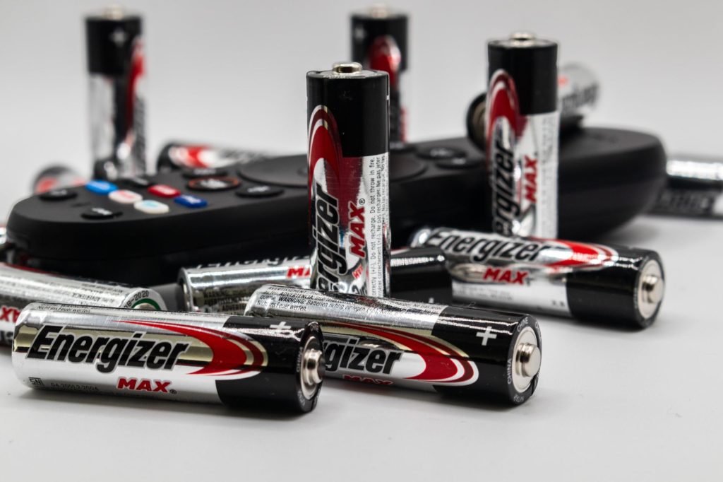 Close-up of multiple Energizer AA batteries and a remote control on a white surface.