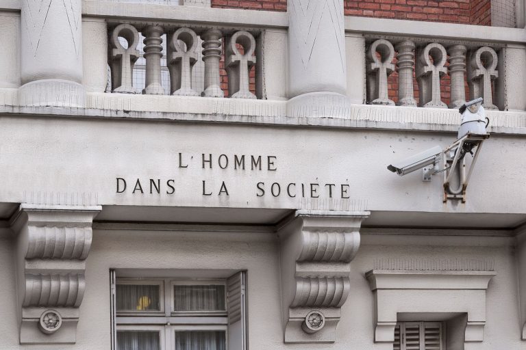 Close-up of a Parisian building facade featuring classic architecture and a surveillance camera.