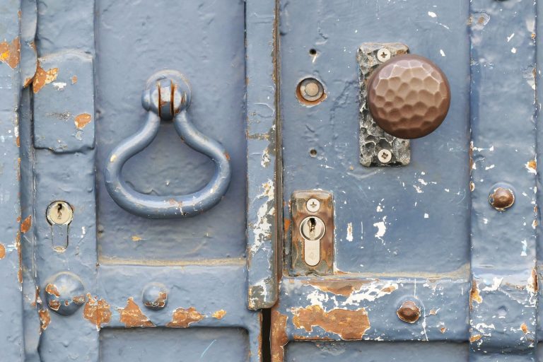 Close-up of a weathered blue door with a vintage knocker and rusty lock.
