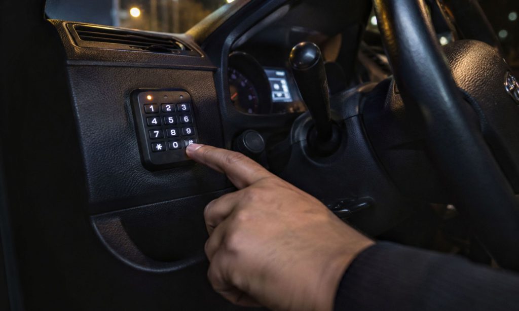 A hand entering code on a car security keypad in a vehicle interior for theft prevention.