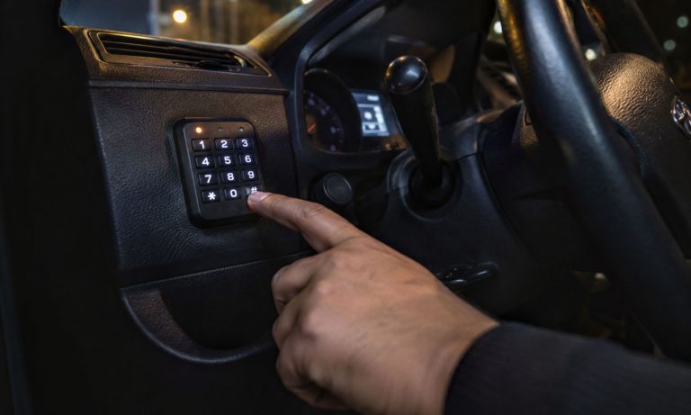 A hand entering code on a car security keypad in a vehicle interior for theft prevention.
