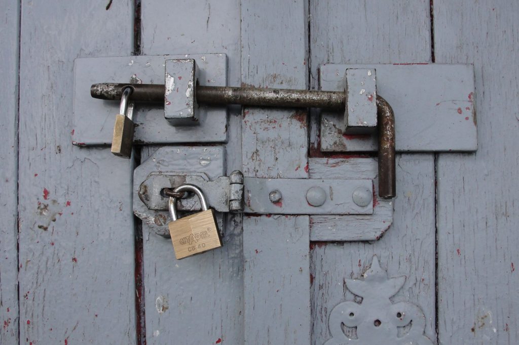 Detailed view of a securely locked wooden door with weathered brass padlocks.