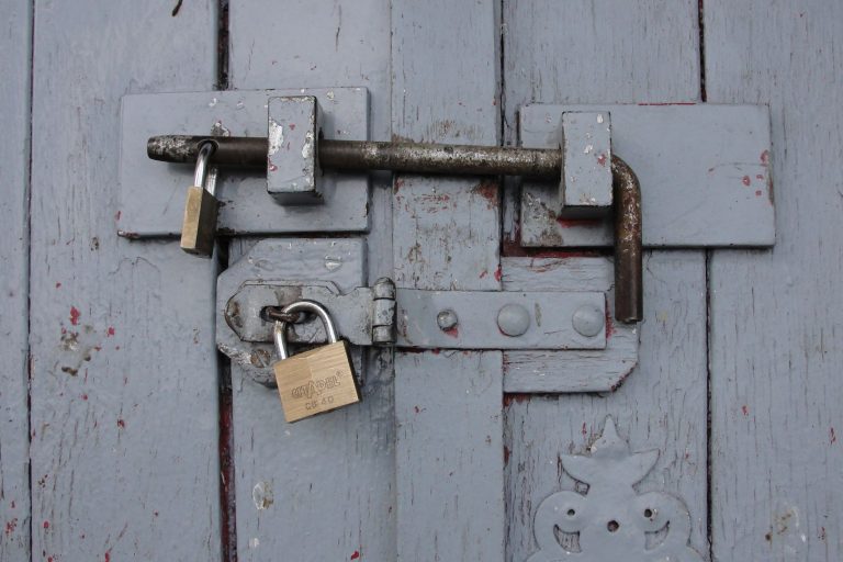 Detailed view of a securely locked wooden door with weathered brass padlocks.