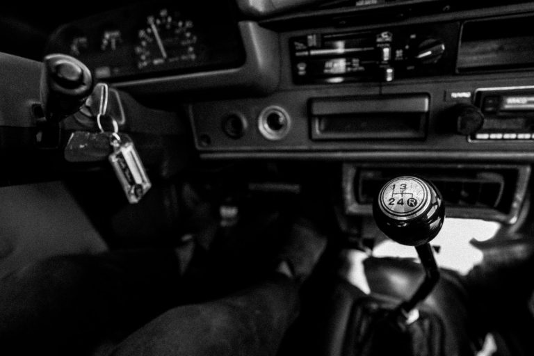 Black and white photo showcasing a vintage car interior with a manual gearshift and dashboard.