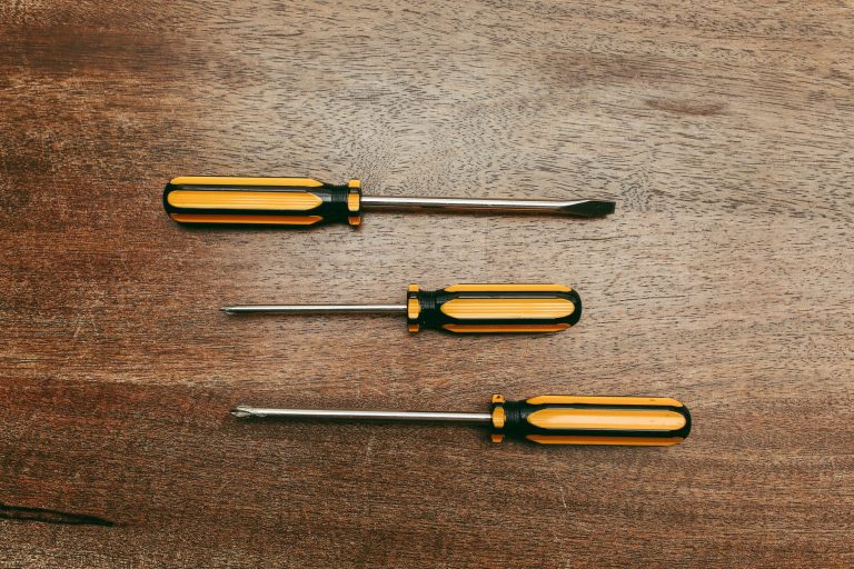 Flat lay of three screwdrivers on a wooden table, showcasing different types.
